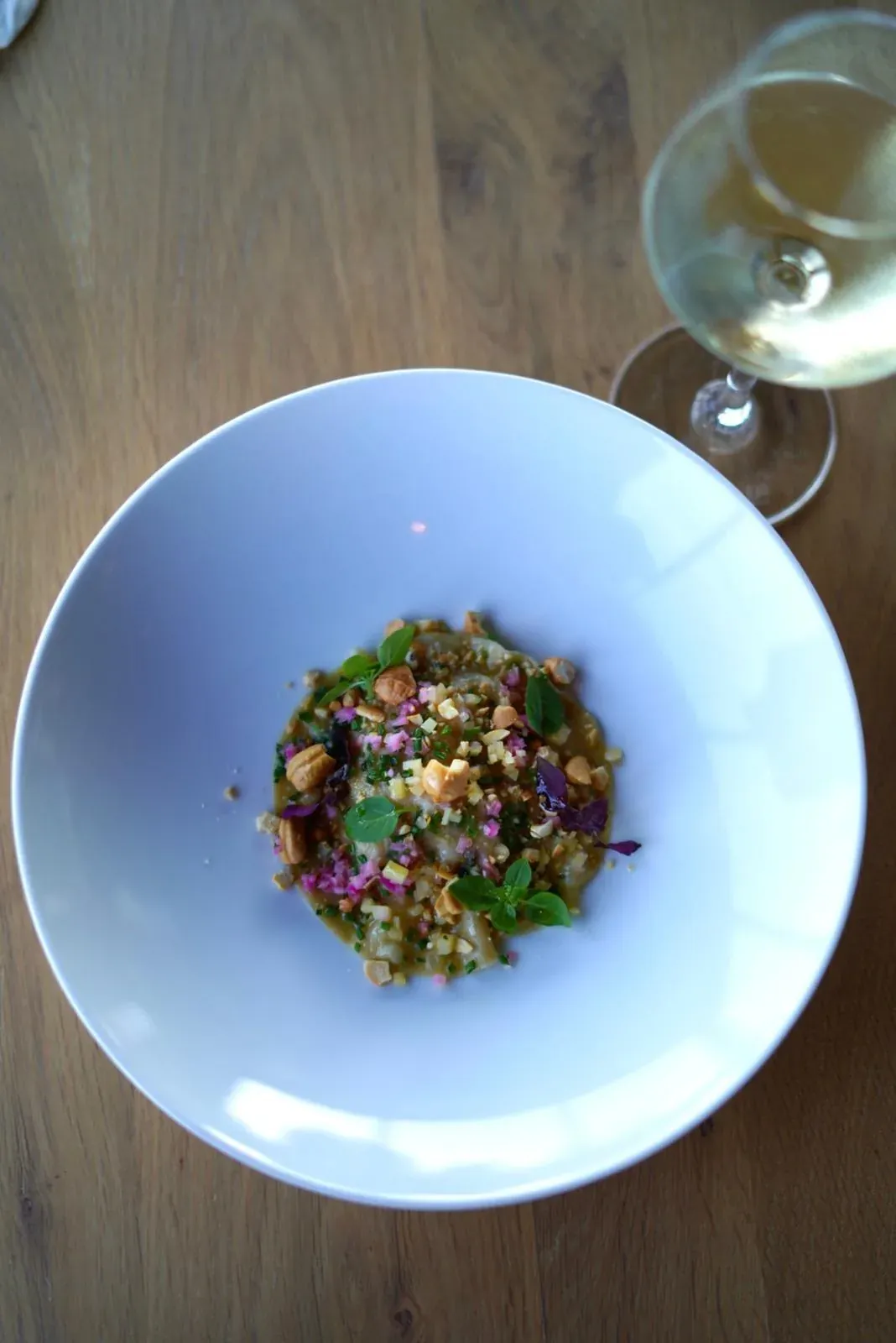 A plated dish on a wooden table beside a glass of white wine